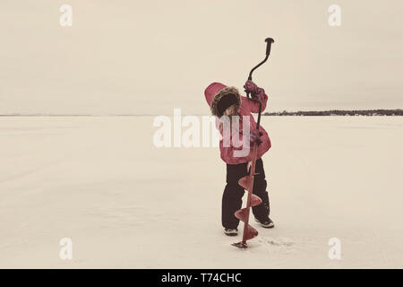 Jeune Fille essayant de percer un trou dans la glace du lac Wabamun congelé sans succès : Wabamun, en Alberta, Canada Banque D'Images