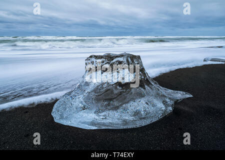 Gros bloc de glace assis sur la rive de l'Islande avec un ciel dramatique en derrière elle, près de la lagune glaciaire du Jökulsárlón ; l'Islande Banque D'Images