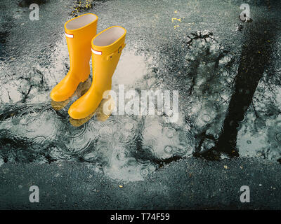 Bottes en caoutchouc jaune dans une flaque d'eau de pluie Banque D'Images