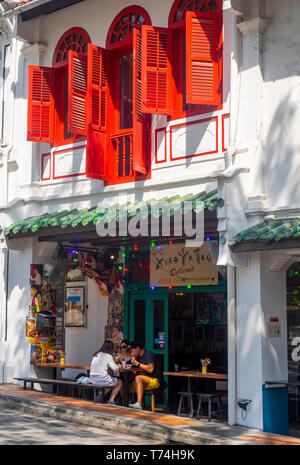 Les habitants de manger en plein air à l'extérieur d'un restaurant dans un magasin traditionnel avec des volets rouges. Banque D'Images