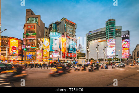 Flou de la moto en passant par carrefour occupé en face du quartier commerçant à Taipei Ximending pendant le crépuscule avec foule de personnes Banque D'Images