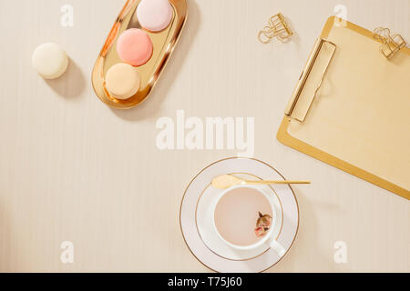 Bureau d'accueil de femmes avec l'espace de presse-papiers, macarons, stylo, tasse de café sur fond pastel. Mise à plat, vue du dessus vie concept. Banque D'Images