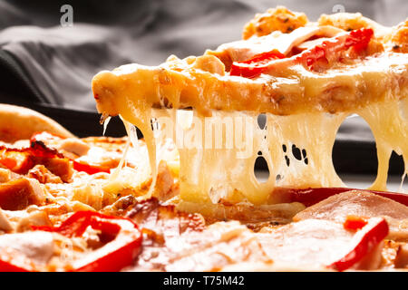 Hot big pizza au pepperoni pizza savoureuse composition avec bacon jambon fromage fusion tomates paprika fumée vapeur sur fond noir Banque D'Images