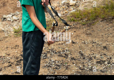 Petit enfant à l'aide de lance-pierres fait main faite avec branche d'arbre et des matériaux recyclés. Enfant à l'aide d'un jouet traditionnel dans un champ dans la nature, débrancher du te Banque D'Images