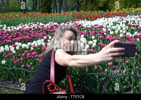 Jeune femme faisant sur la pelouse selfies en face de tulipes colorées. Le 25 avril 2019. Parc du chant. Kiev, Ukraine Banque D'Images