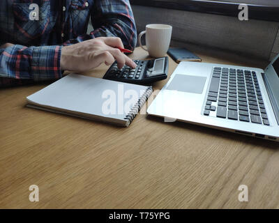 Un homme comptable travaille à un ordinateur à la maison, compte sur une calculatrice et prend des notes sur un ordinateur portable, un indépendant au travail, de l'espace libre pour le texte. Banque D'Images