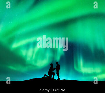 Aurora Borealis et silhouette d'un homme faire de demande en mariage à sa petite amie. Paysage de nuit avec northern lights, ciel étoilé et les amoureux. Coupl Banque D'Images