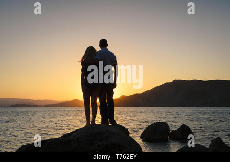 Le gars et la fille s'ouvrent en regardant le coucher du soleil. Silhouette d'un couple in love Banque D'Images