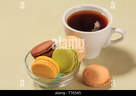 De savoureux gâteaux macarons de couleur différente dans la cuvette en verre et tasse de café sur fond beige. Banque D'Images