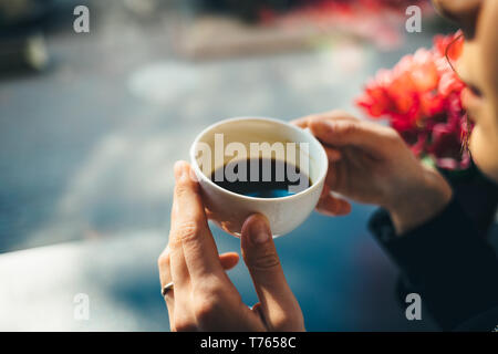 Tasse de café dans woman's hands, close-up. Girl drinking espresso à la table près de fenêtre dans cafe sur matin ensoleillé. Banque D'Images