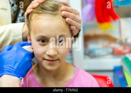 Girl pierced oreille dans le salon de beauté. Adorable petite fille ayant le perçage des oreilles processus avec équipement spécial dans le centre de beauté par un professionnel de la santé. Banque D'Images