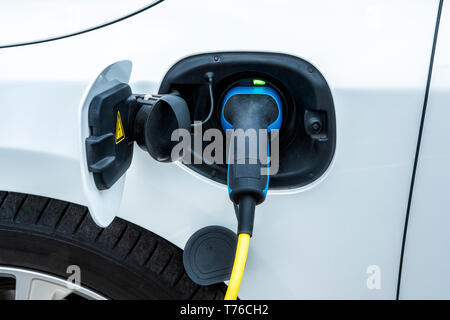 La voiture électrique est en cours de chargement à station de charge, et un gros plan de l'alimentation est branché dans une prise électrique. Banque D'Images