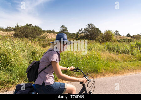 Femme blonde rire avec lunettes de soleil et chapeau sur un vélo entre les champs de la mer du Nord Banque D'Images