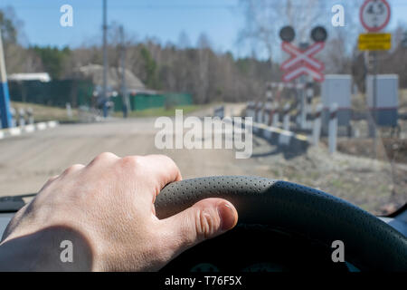 Vue de la main du conducteur sur le volant de la voiture, qui s'est arrêté avant le passage à niveau et l'indicateur de signalisation routière Banque D'Images