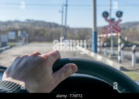 Vue de la main du conducteur sur le volant de la voiture, qui s'est arrêté avant le passage à niveau et l'indicateur de signalisation routière Banque D'Images