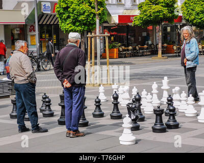 Neuwied, Rhénanie-Palatinat, Allemagne - le 2 mai 2019 : deux hommes jouant aux échecs en plein air sur une place centrale dans la ville avec un spectateur Banque D'Images