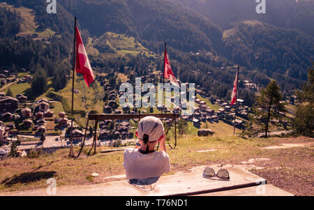 Jeune garçon assis au point d'observation plus alpine village Zinal en été à table en bois avec des lunettes de soleil. Vacances d'été dans les Alpes. Le Canton du Valais, sw Banque D'Images