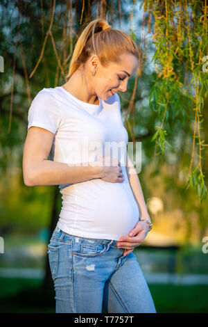 Portrait d'un fier et heureux à la jeune femme enceinte à son ventre en stationnement au lever du soleil, nouveau concept de vie Banque D'Images