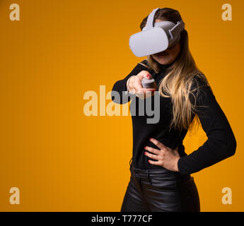 Jeune femme brune portant des lunettes de réalité virtuelle en technologie de l'avenir, d'interaction et souriant tout en jouant, fond jaune, vr conc Banque D'Images