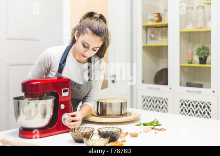Jeune femme pâtissier bat la crème dans un bol en métal rouge dans un mélangeur électrique. Le concept de pâtisserie maison, la cuisine Banque D'Images