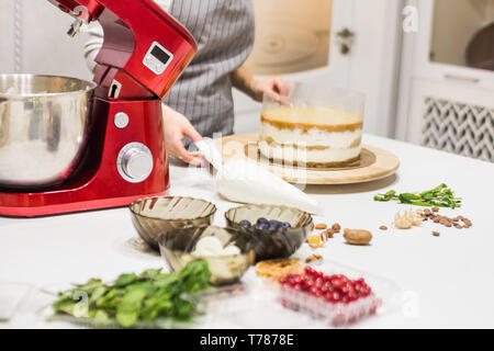 Jeune femme pâtissier bat la crème dans un bol en métal rouge dans un mélangeur électrique. Le concept de pâtisserie maison, la cuisine Banque D'Images