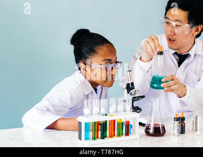 Close-up d'hommes de science de l'Asie et de l'enseignement enseignant alchimiste faisant l'essai de laboratoire de chimie aux curieux African American élève d'école élémentaire Banque D'Images