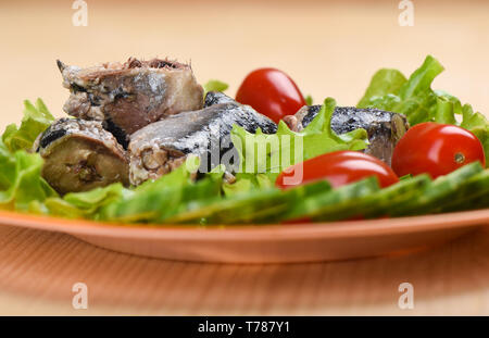 Soft focus. Sardines en conserve iwashi tranchés sur des feuilles de laitue avec concombres et tomates. Style rustique. Copy space Banque D'Images