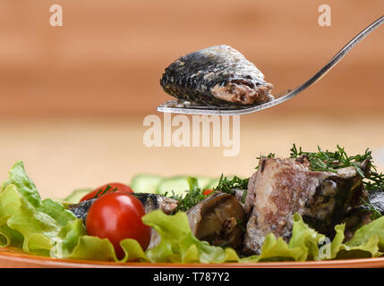 Un morceau de sardine en conserve sur une fourchette au-dessus d'une assiette de sardines et légumes. Copier l'espace. Style rustique. Banque D'Images