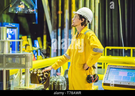 Jeune homme dans un uniforme de travail jaune, les lunettes et le casque dans un environnement industriel, plate-forme d'huile ou de gaz liquéfié plant Banque D'Images