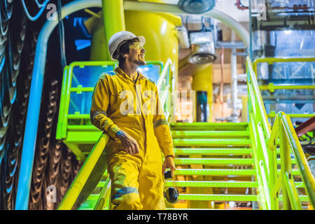 Jeune homme dans un uniforme de travail jaune, les lunettes et le casque dans un environnement industriel, plate-forme d'huile ou de gaz liquéfié plant Banque D'Images