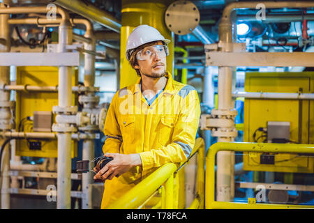 Jeune homme dans un uniforme de travail jaune, les lunettes et le casque dans un environnement industriel, plate-forme d'huile ou de gaz liquéfié plant Banque D'Images