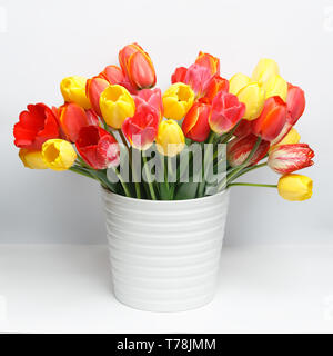 Grand bouquet de tulipes jaunes et rouges debout dans un grand vase blanc sur un tableau blanc Banque D'Images