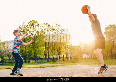 Deux jeunes garçons pratiquent leur compétences en basket-ball chaude soirée de lumière sur un terrain de sport avec un saut pour éviter les mouvements de défense de la deuxième Banque D'Images