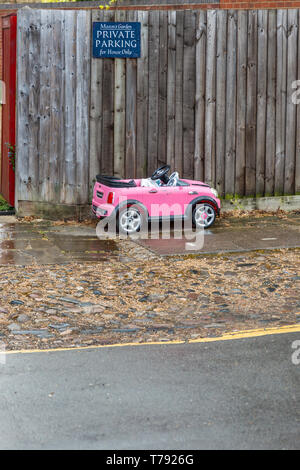 Image d'humour d'un petit jouet enfant voiture garée en dessous d'un parking privé. Vu à Cambridge, Angleterre, Royaume-Uni. Banque D'Images