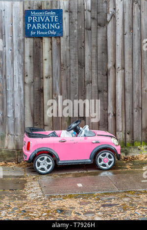 Image d'humour d'un petit jouet enfant voiture garée en dessous d'un parking privé. Vu à Cambridge, Angleterre, Royaume-Uni. Banque D'Images