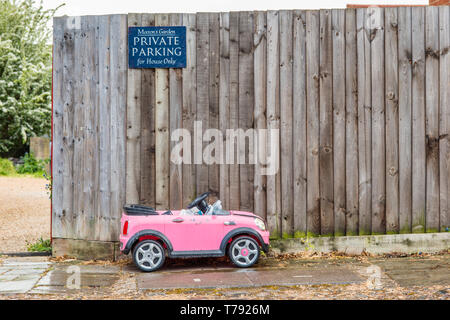 Image d'humour d'un petit jouet enfant voiture garée en dessous d'un parking privé. Vu à Cambridge, Angleterre, Royaume-Uni. Banque D'Images