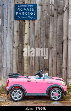 Image d'humour d'un petit jouet enfant voiture garée en dessous d'un parking privé. Vu à Cambridge, Angleterre, Royaume-Uni. Banque D'Images