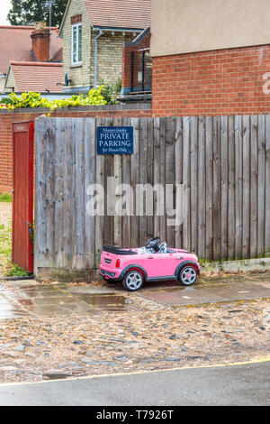 Image d'humour d'un petit jouet enfant voiture garée en dessous d'un parking privé. Vu à Cambridge, Angleterre, Royaume-Uni. Banque D'Images