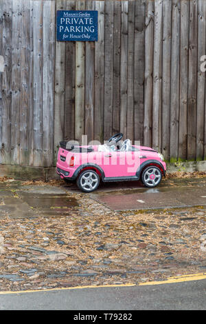 Image d'humour d'un petit jouet enfant voiture garée en dessous d'un parking privé. Vu à Cambridge, Angleterre, Royaume-Uni. Banque D'Images