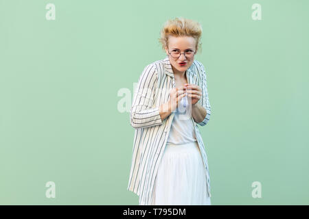 Portrait de jeune femme blonde drôle en chemise blanche, jupe et chemisier rayé avec lunettes debout avec ruse et face à la route. Piscine stu Banque D'Images