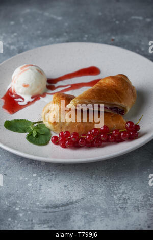 Des tranchées d'un strudel aux fruits rouges frais servi avec des baies de cassis et le sucre en poudre sur une vieille plaque de fond sur un pic avec de la crème glacée Banque D'Images