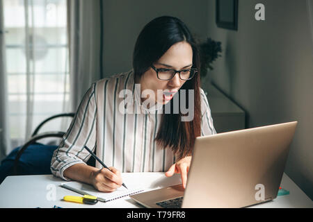 Une belle jeune fille n'élève ses devoirs ou travaille dans un bureau à domicile. Il est surpris par l'actualité ou elle a trouvé une solution inédite. Banque D'Images