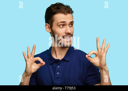 Drôle homme séduisant montrant ring signe. cute reliant le pouce et l'index dans un cercle. isolé sur fond bleu. Banque D'Images