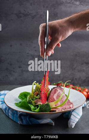 La décoration de la main du chef salade de viande par des pinces de cuisine. cuisine gastronomique. vertical concept Banque D'Images