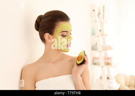 Belle jeune femme avec un masque facial et avocat frais à la maison Banque D'Images