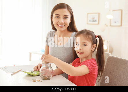 Petite fille avec sa mère assis à table et de l'argent comptant à l'intérieur. Concept d'épargne de l'argent Banque D'Images