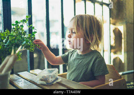 Un petit enfant est assis à une table de restaurant en plein air avec la nourriture apportée de la maison Banque D'Images