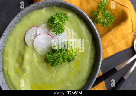 Soupe crème de brocoli avec le radis et cuillère sur plaques gris, avec serviette orange sur fond gris. Le brocoli cru frais près de. Concept d'alimentation saine. Fla Banque D'Images