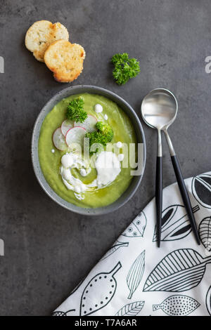 Soupe de crème chaude avec brocoli et la crème dans un bol et le radis, du pain et une cuillère à fond gris, serviette blanche près de l'arrière-plan sur le béton. Concept de il Banque D'Images