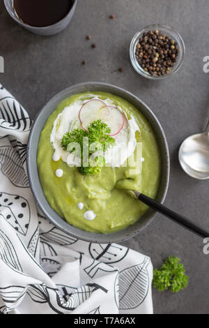 Close up crème délicieuse soupe avec le brocoli et la crème et dans un bol de radis, du pain et une cuillère à fond gris, serviette blanche près de l'arrière-plan sur le béton. Co Banque D'Images